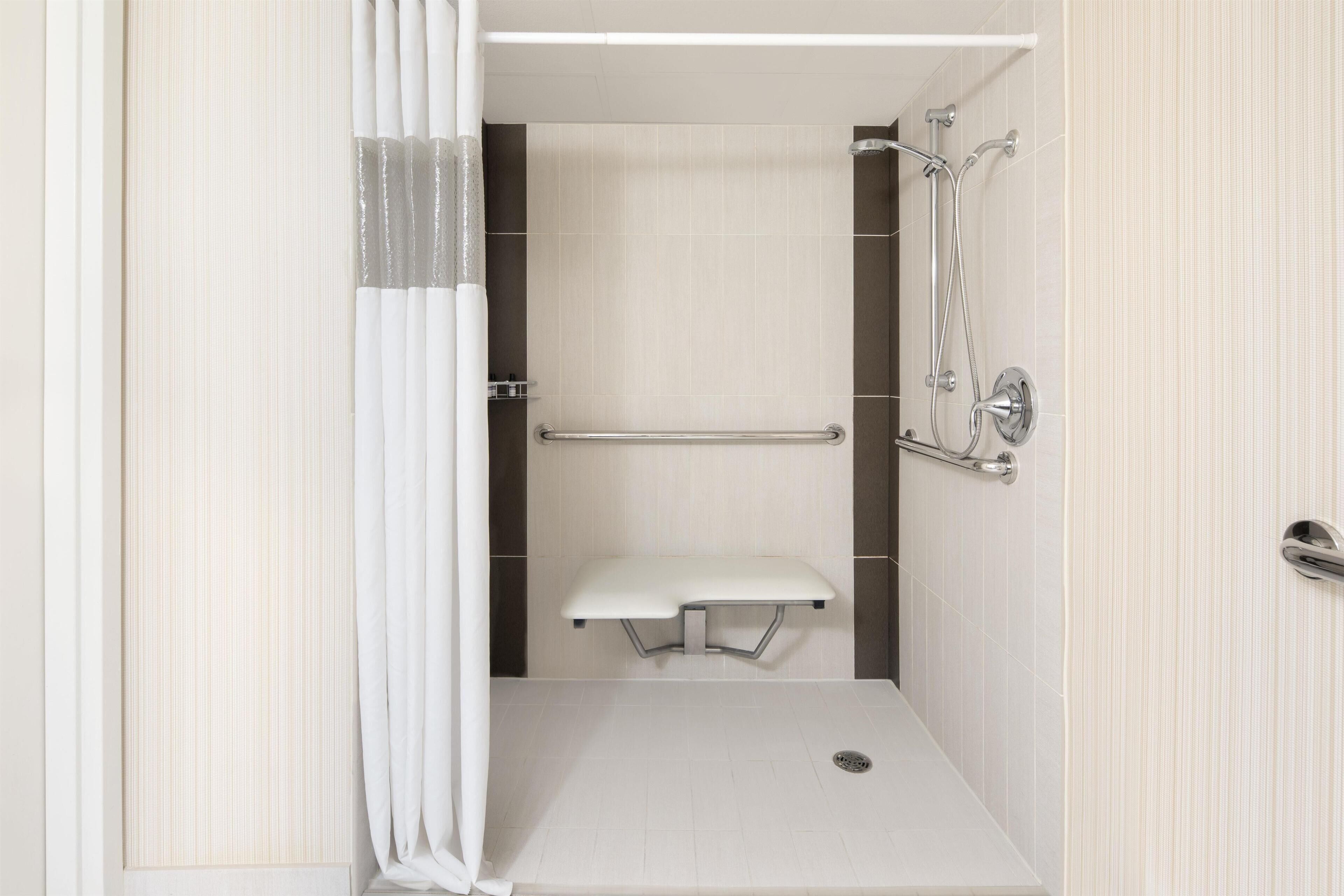 A walk-in shower with a bench, grab bars, and a showerhead.