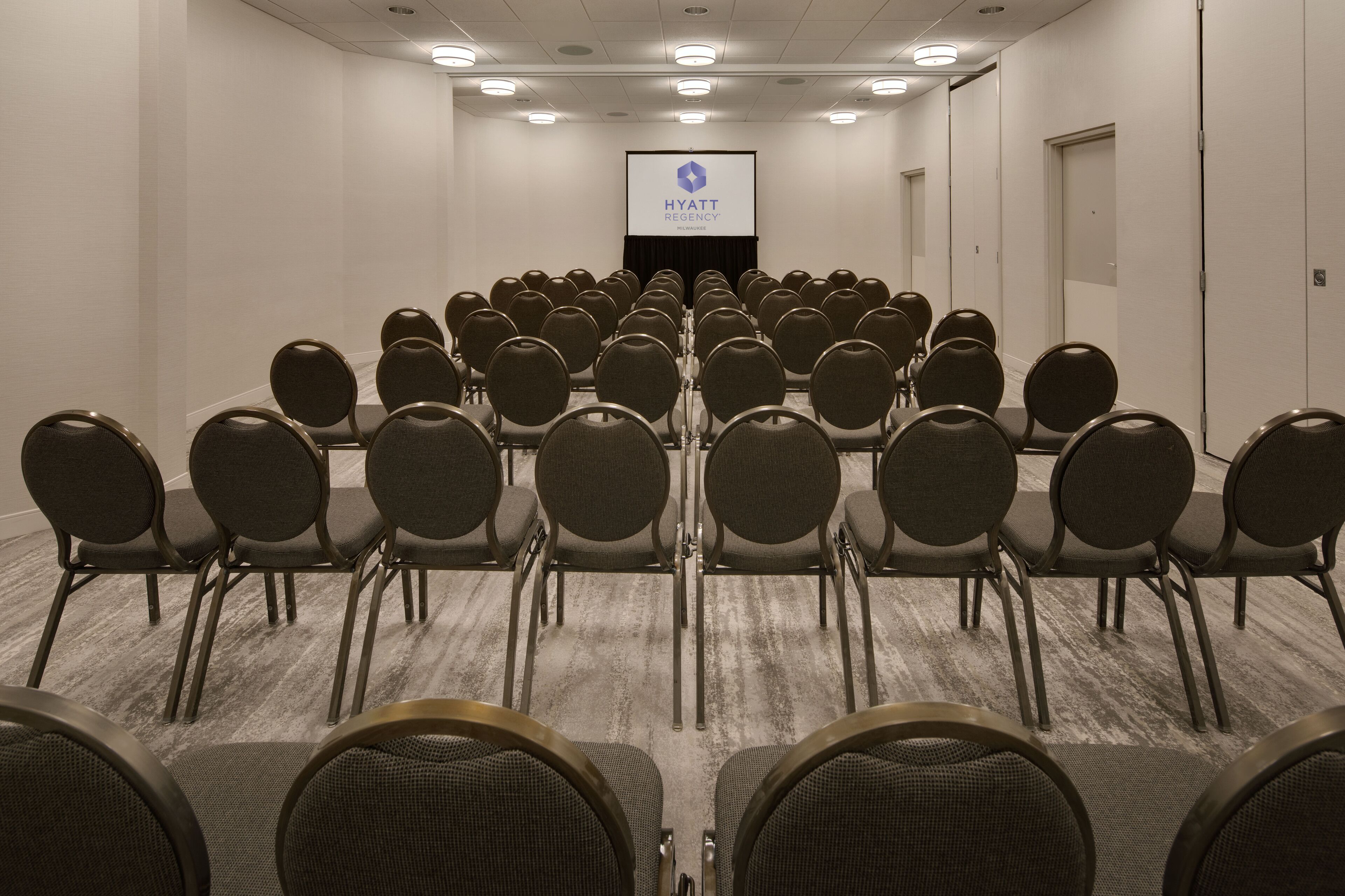 Un salón de conferencias con filas de sillas mirando una pantalla de proyección que muestra el logotipo de Hyatt Regency.