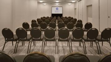 Un salón de conferencias con filas de sillas mirando una pantalla de proyección que muestra el logotipo de Hyatt Regency.