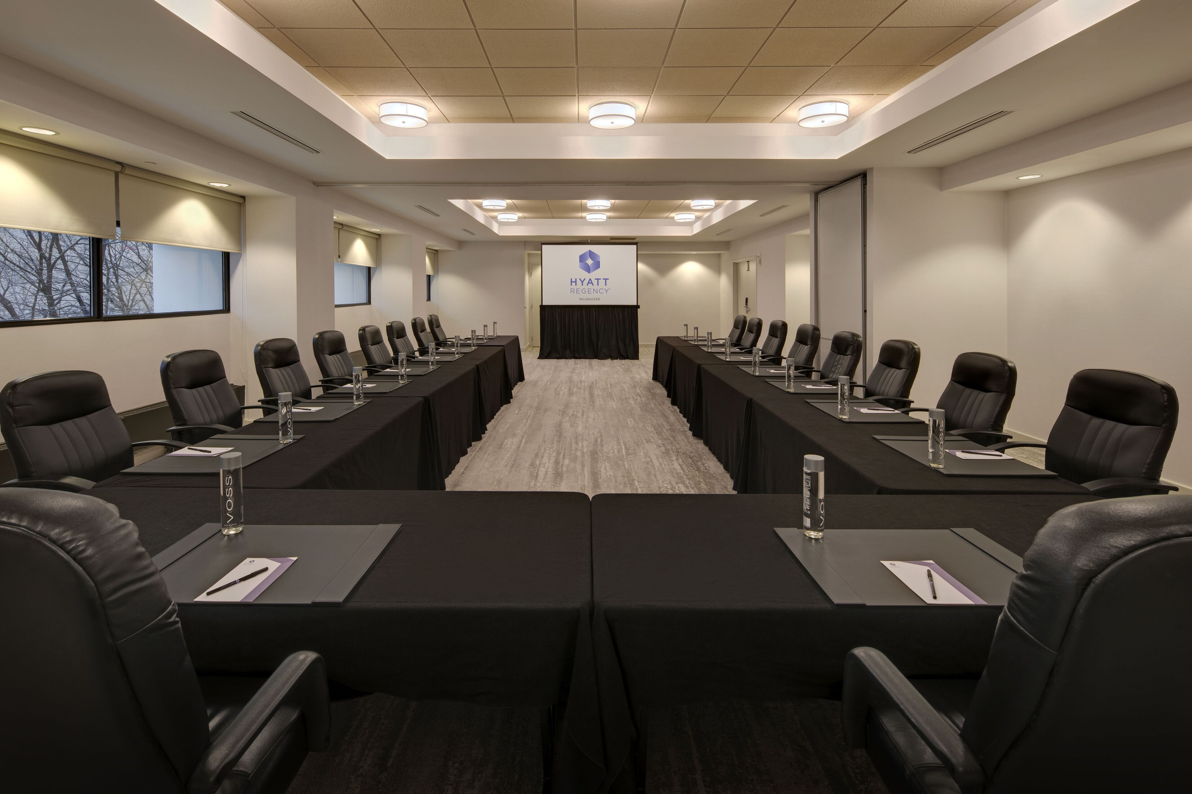 A conference room with a long table, black leather chairs, and a screen displaying the Hyatt Regency logo.