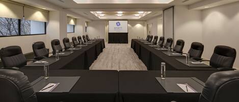 A conference room with a long table, black leather chairs, and a screen displaying the Hyatt Regency logo.