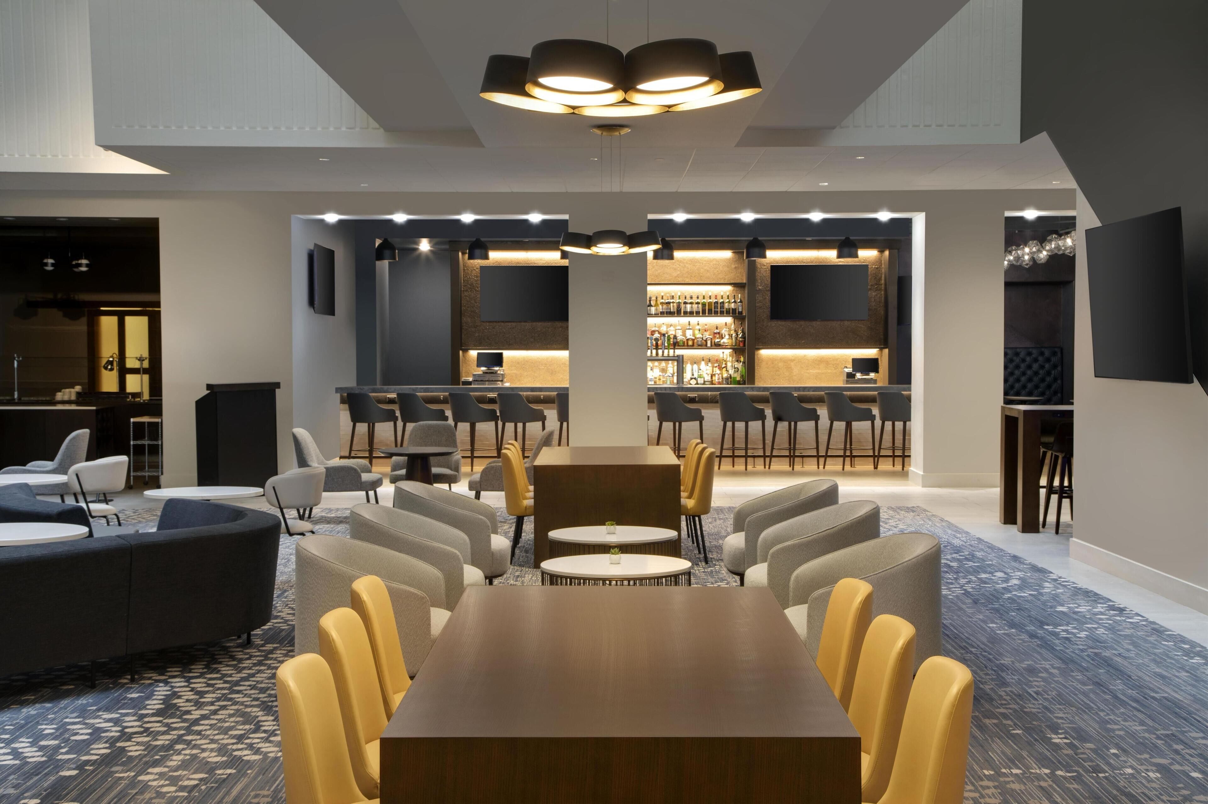 Un moderno vestíbulo de hotel con un área de estar central, un bar y una pantalla grande.