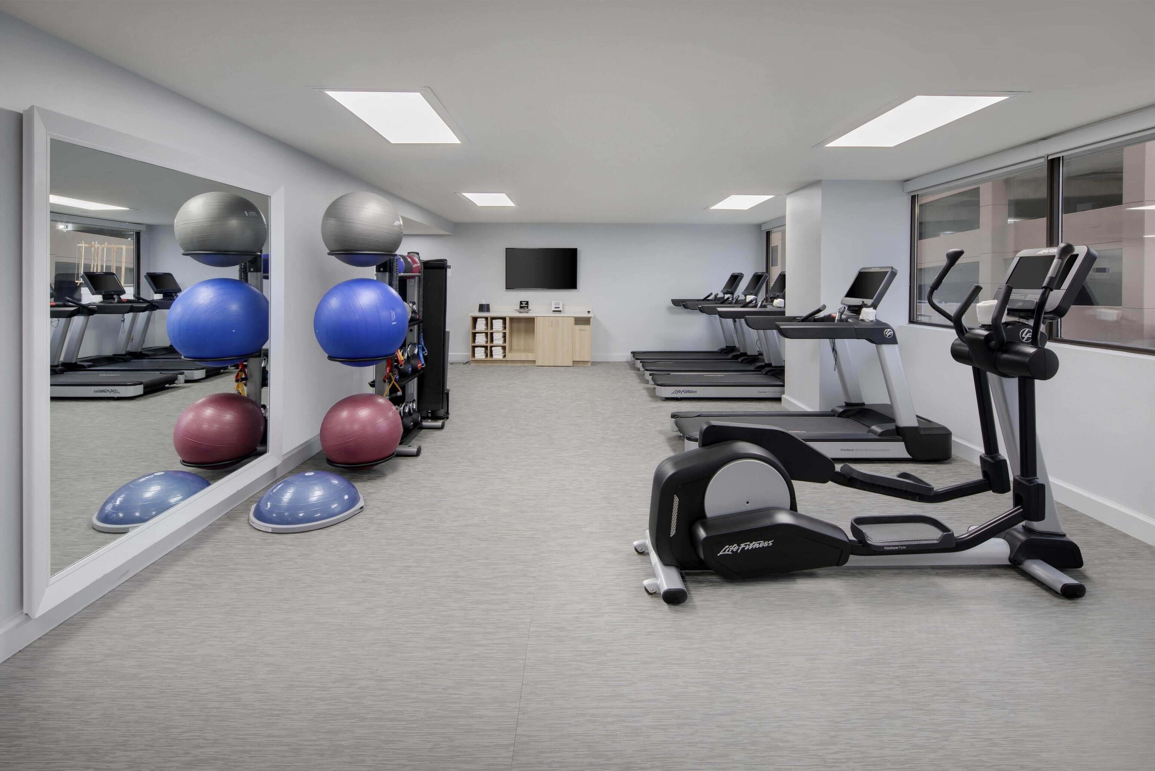 A gym with treadmills, elliptical machines, and exercise balls.
