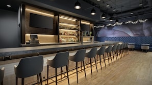 A bar area with a long counter, multiple stools, and a wall-mounted TV.