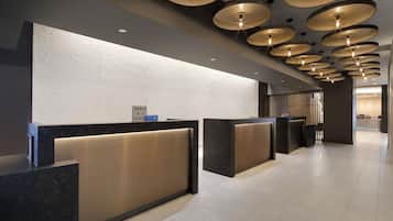 Zona d'entrada d'un hotel modern amb un mostrador central, diverses finestres d'atenció al client i un sostre decoratiu amb llums circulars.
