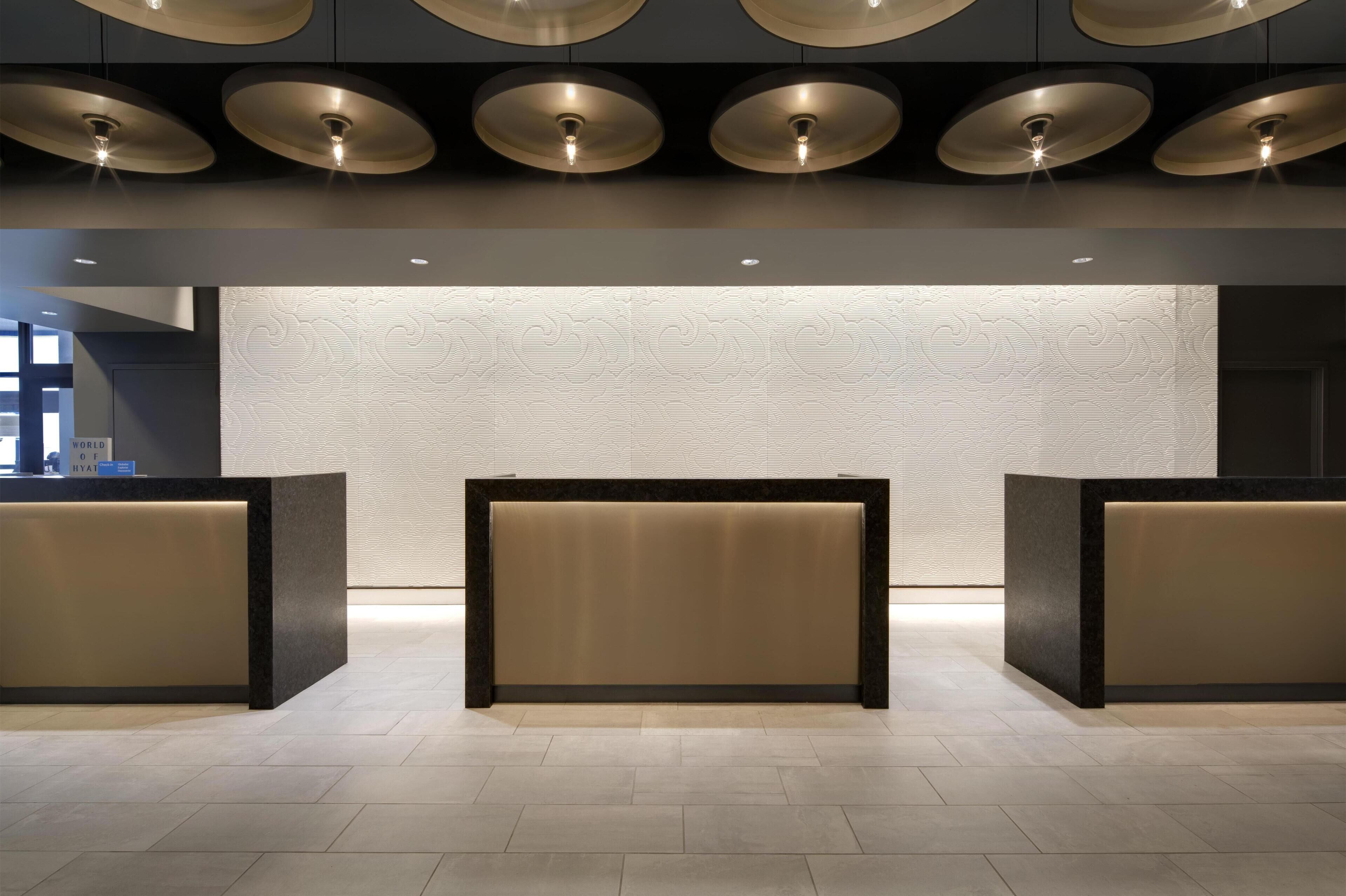 A reception area with a modern design, featuring a central reception desk flanked by two smaller desks, a textured wall behind, and a series of circular ceiling lights.