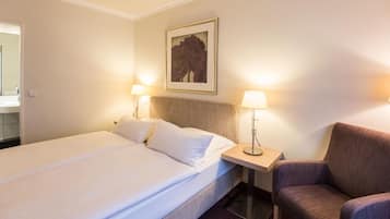Una habitación de hotel con una cama, dos lámparas de noche, una silla y un cuadro en la pared.