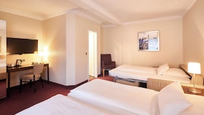 Een hotelkamer met drie bedden, een bureau met stoel, een televisie en een schilderij aan de muur.