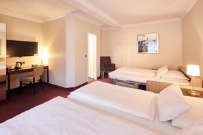 Une chambre d’hôtel avec trois lits, un bureau avec une chaise, une télévision et un tableau au mur.