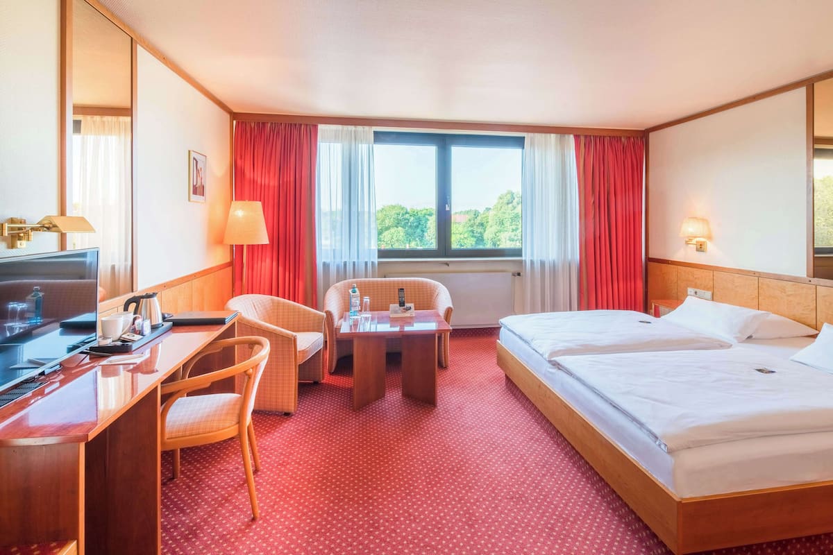 Een hotelkamer met een bureau, twee stoelen, een tafeltje, een bed en een raam met gordijnen.
