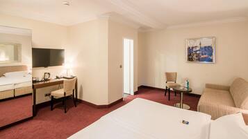 A hotel room with a bed, a desk with a chair, a television, a painting on the wall, and a small table with a chair.