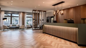 Een moderne hotel lobby met een receptiebalie, zithoek en grote ramen.