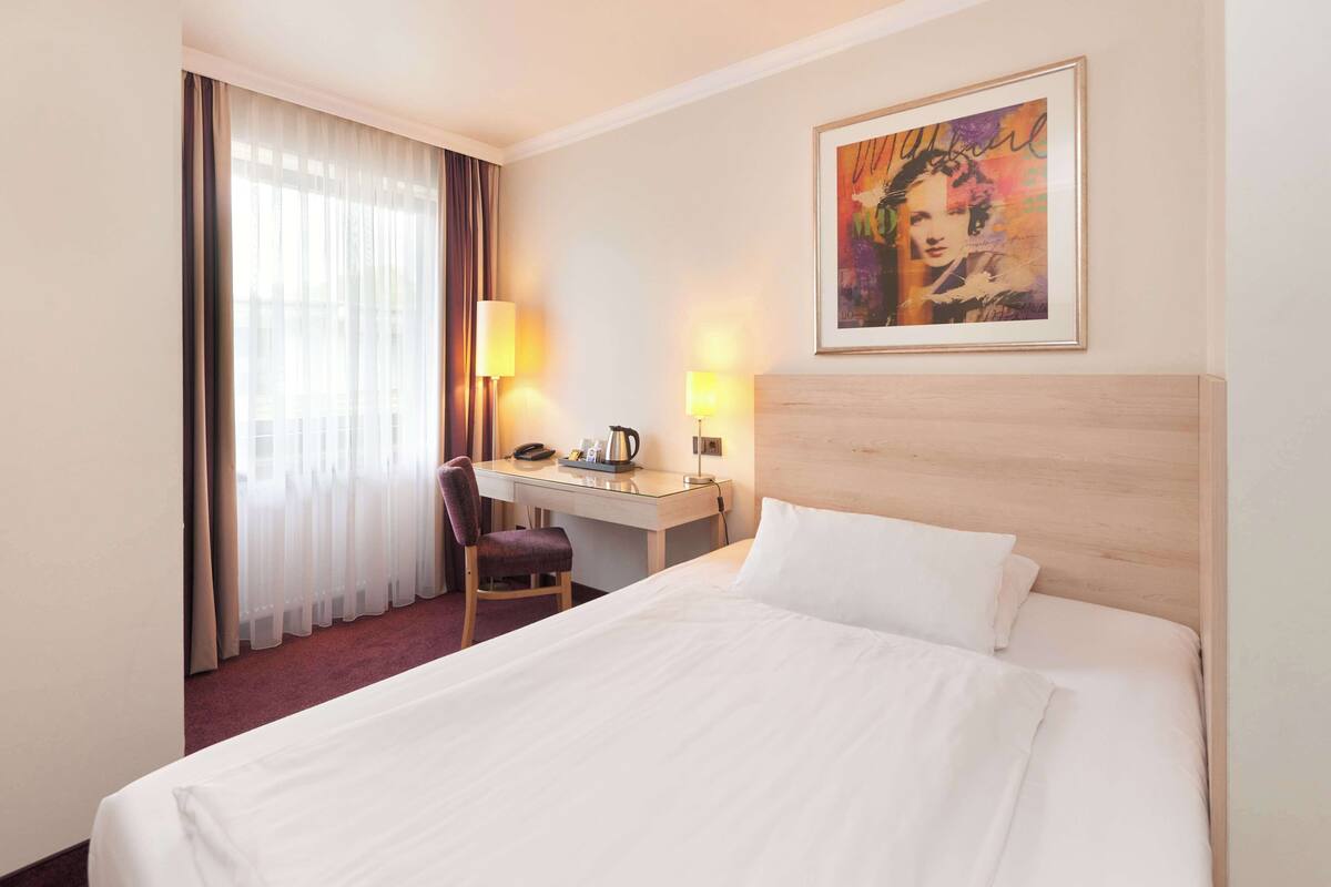 Een hotelkamer met een bed, bureau, stoel en een schilderij aan de muur.