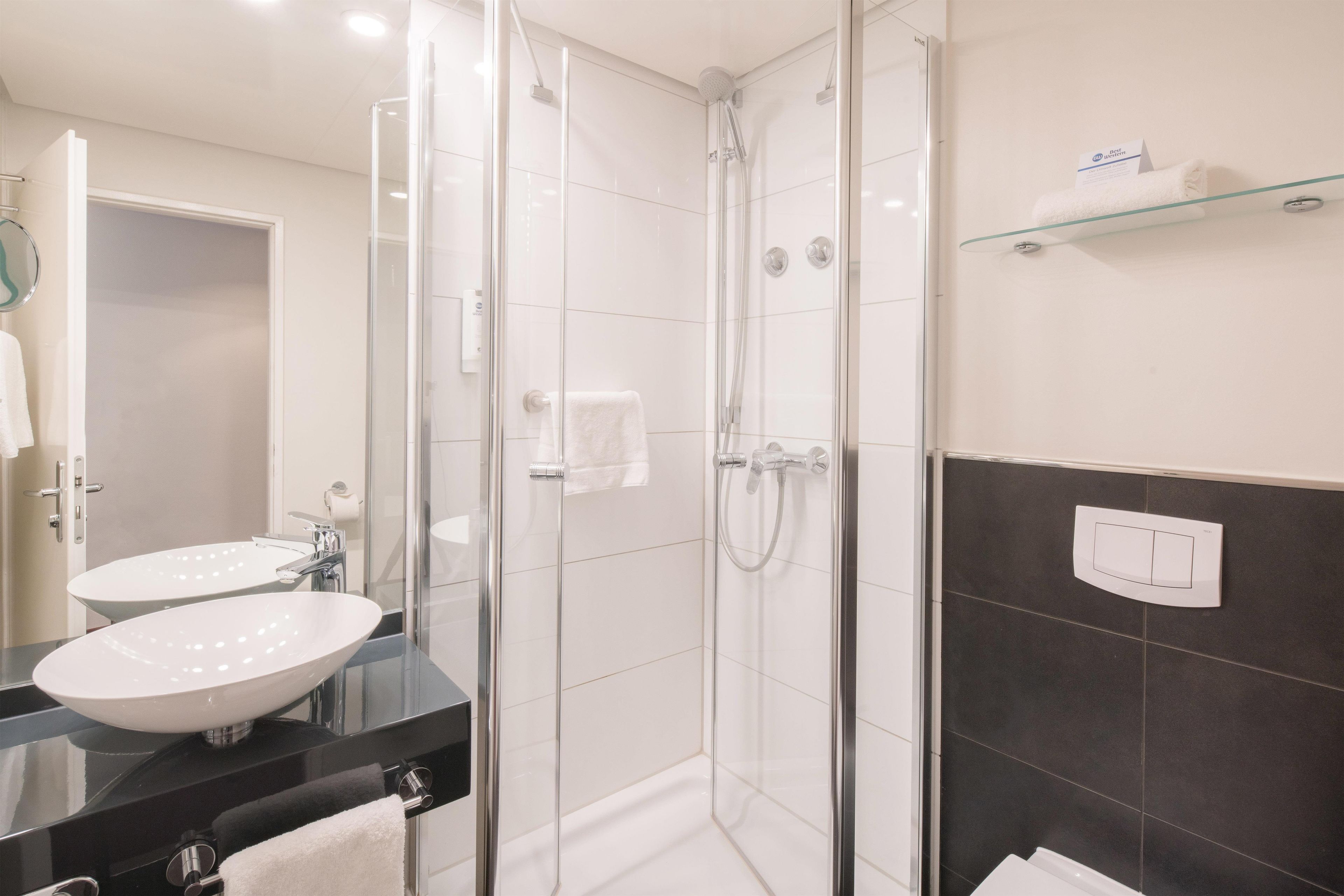 A modern bathroom with a glass-enclosed shower, a white sink, and a glass shelf.