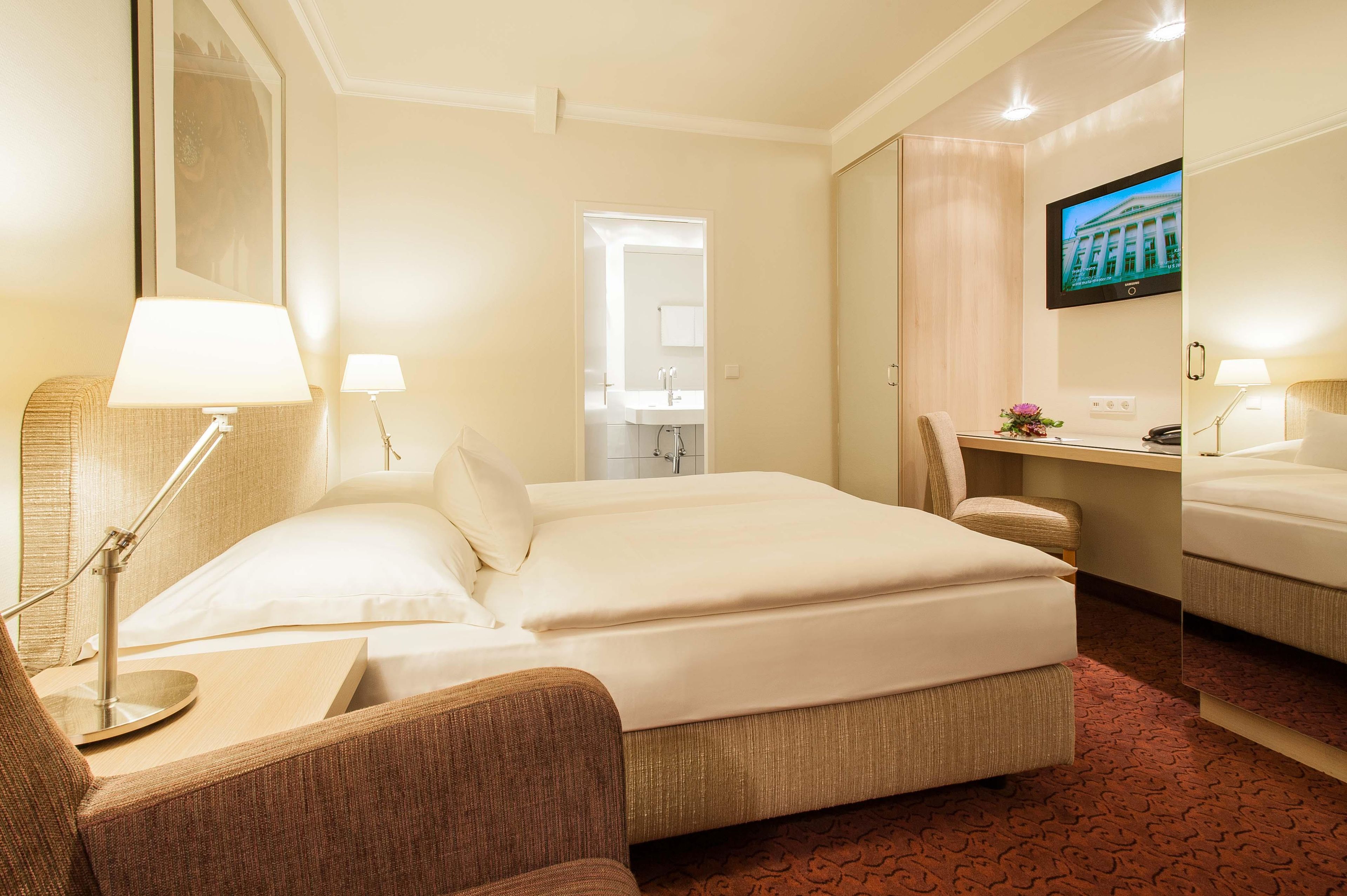 Ein Hotelzimmer mit Bett, Schreibtisch, Stuhl, Fernseher und Spiegel.
