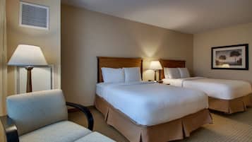A hotel room with two beds, a chair, a lamp, and a picture on the wall.