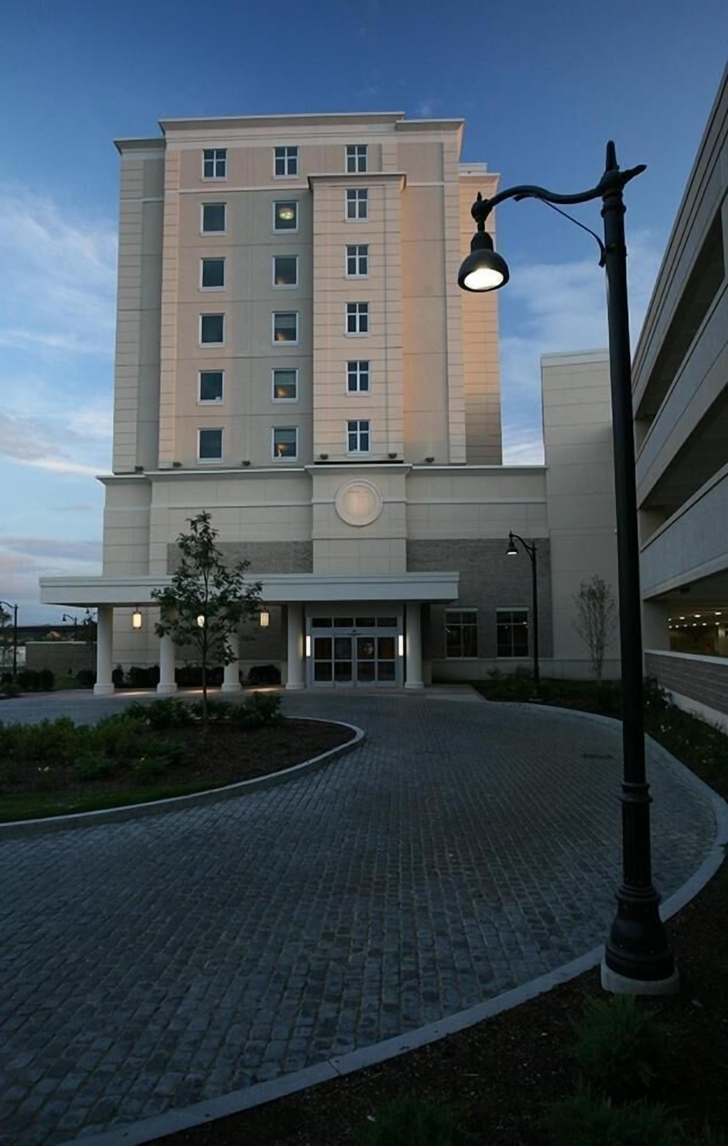A multi-story hotel with a central entrance, a paved driveway, and a street lamp.
