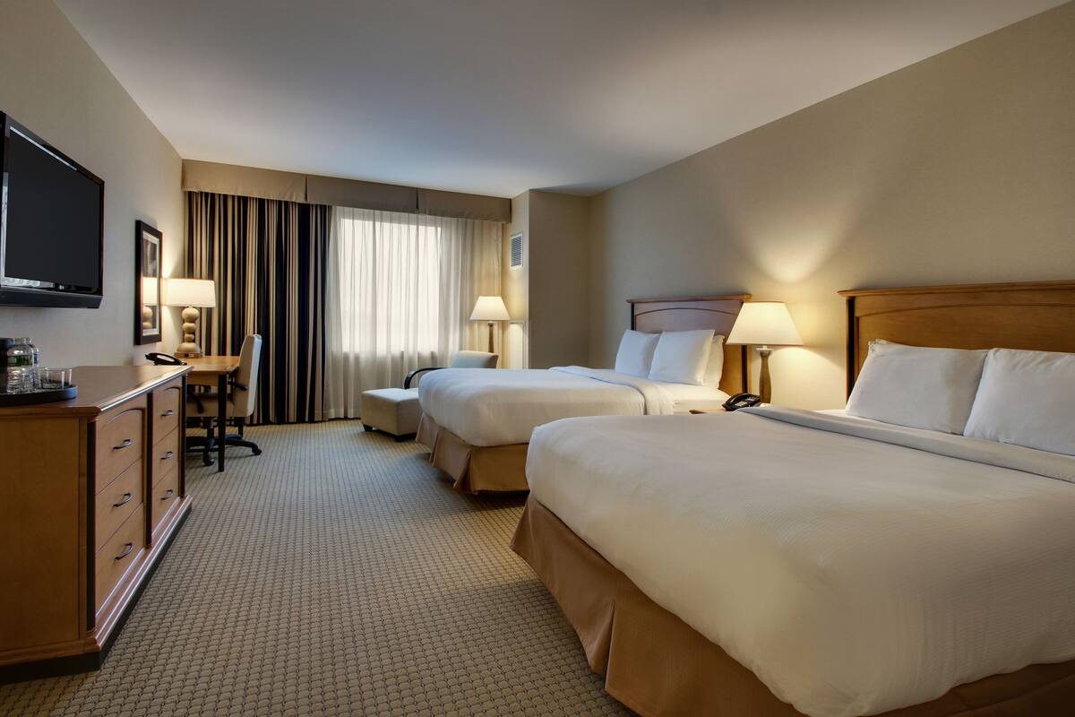 Een hotelkamer met twee bedden, een bureau, een stoel, een televisie en een raam met gordijnen.