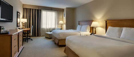 Une chambre d’hôtel avec deux lits, un bureau, une chaise, une télévision et une fenêtre avec des rideaux.
