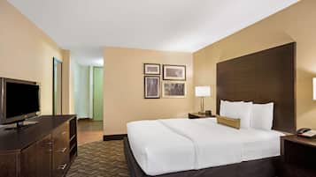 Habitación de hotel con una cama grande, un televisor en una cómoda, cuadros en la pared y una mesita de noche con una lámpara.