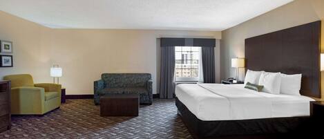 A hotel room with a large bed, a sofa, a chair, and a desk.