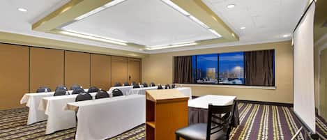 Un salón de conferencias con mesas, sillas, un atril y una pantalla para proyecciones.