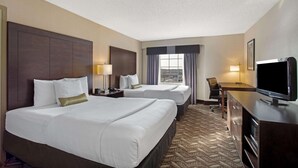 Une chambre d’hôtel avec deux lits, un bureau, une télévision et une fenêtre avec des rideaux.