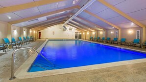 Une piscine intérieure à l’eau d’un bleu limpide, entourée de chaises et dotée d’un plafond haut laissant apparaître les conduits de ventilation.