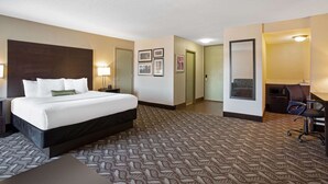 A hotel room with a large bed, a desk, and a chair. There are framed pictures on the wall and a door leading to another room.