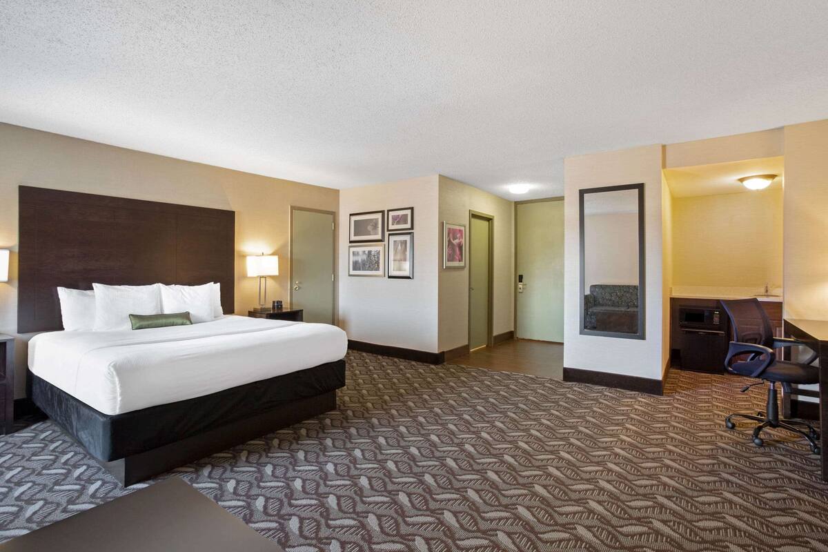 Habitación de hotel con una cama grande, un escritorio y una silla. Hay cuadros en la pared y una puerta que da a otra habitación.