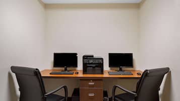A small office with two desks, each with a computer monitor, keyboard, and mouse. There are two black office chairs, a printer, and a filing cabinet.