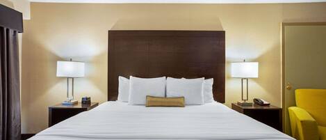 A hotel room with a large bed, two bedside tables, a nightstand, a lamp, a chair, and a mirror.