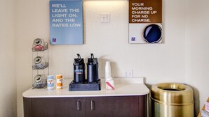 A hotel room with a counter displaying coffee makers, sugar, and cream containers. There are two motivational signs on the wall, one about leaving the light on and the other about no morning charge.