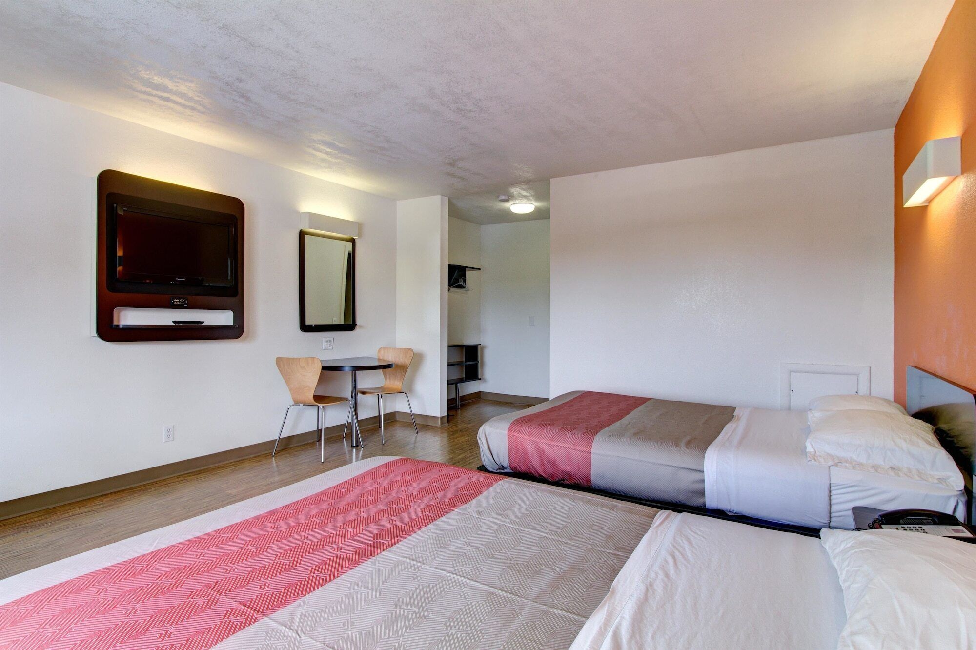 A hotel room with two beds, a desk, a chair, a mirror, and a television.
