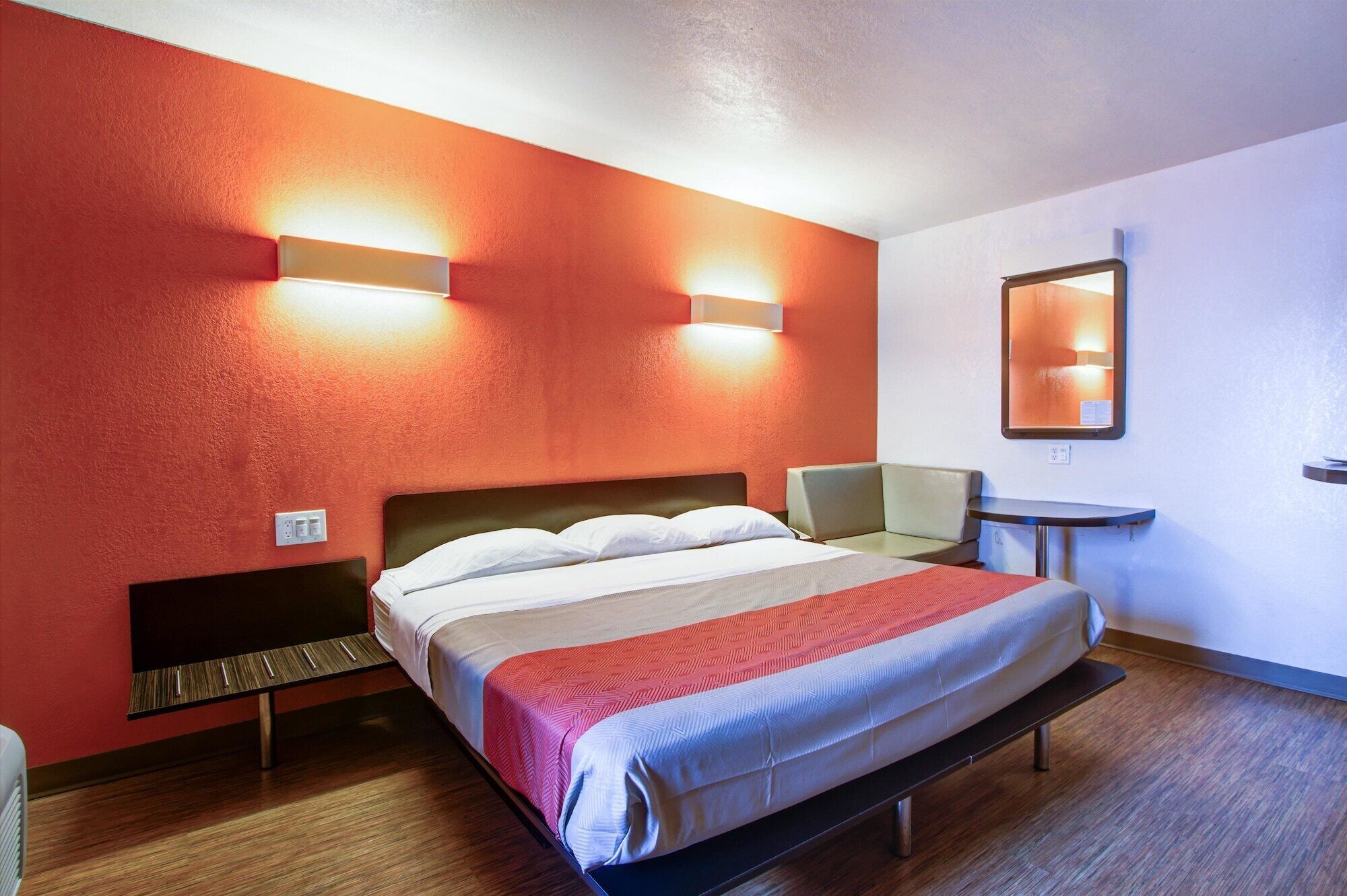 Een hotelkamer met een bed, een stoel, een klein tafeltje en een spiegel aan de muur.