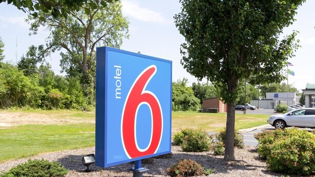 A motel sign with the number 6, surrounded by landscaped bushes and trees.