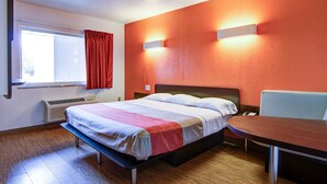 A hotel room with a bed, a desk, a chair, a window with curtains, and a wall-mounted heater.