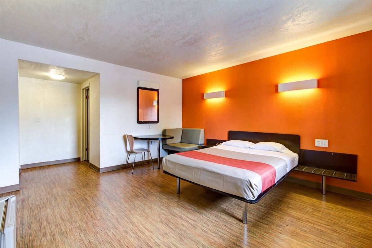 Une chambre d’hôtel avec un lit, un bureau et une chaise. Une porte donne accès à une autre pièce.
