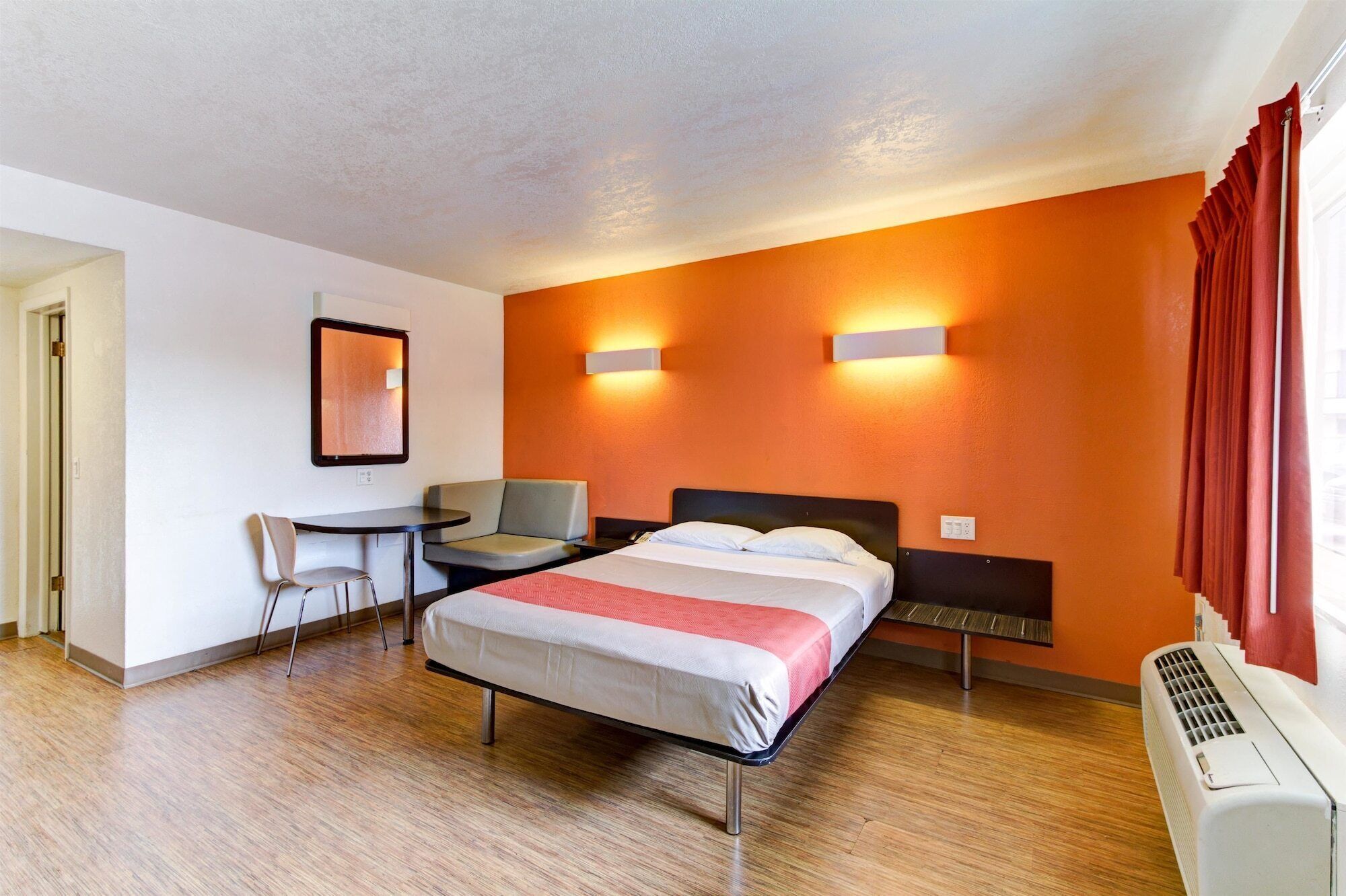 A hotel room with a bed, a desk, a chair, and a heater.