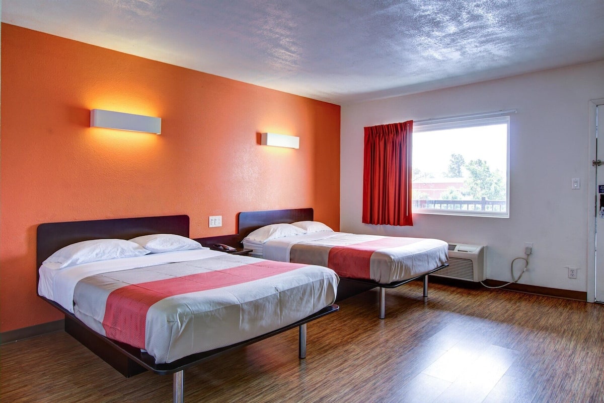 Une chambre d’hôtel avec deux lits, une fenêtre avec des rideaux rouges et un radiateur fixé au mur.