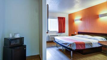 A hotel room with a bed, a desk with a microwave, a window with curtains, and a wall-mounted light.