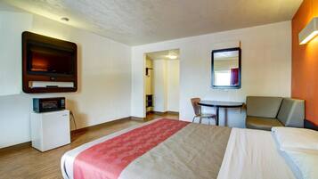 A hotel room with a bed, a desk, a chair, a microwave, and a television.