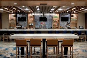 A modern bar area with a long counter, multiple seating options, and a variety of liquor bottles. - Delta Hotels by Marriott Utica (Utica)