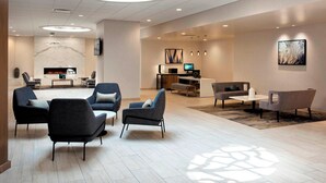 A modern hotel lobby with a seating area, a reception desk, and a television. - Delta Hotels by Marriott Utica (Utica)