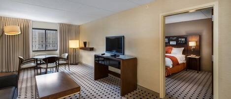 Ein Hotelzimmer mit einem Bett, einem Schreibtisch mit Fernseher, einer Sitzecke mit Stühlen und Blick auf die Stadt durch das Fenster.