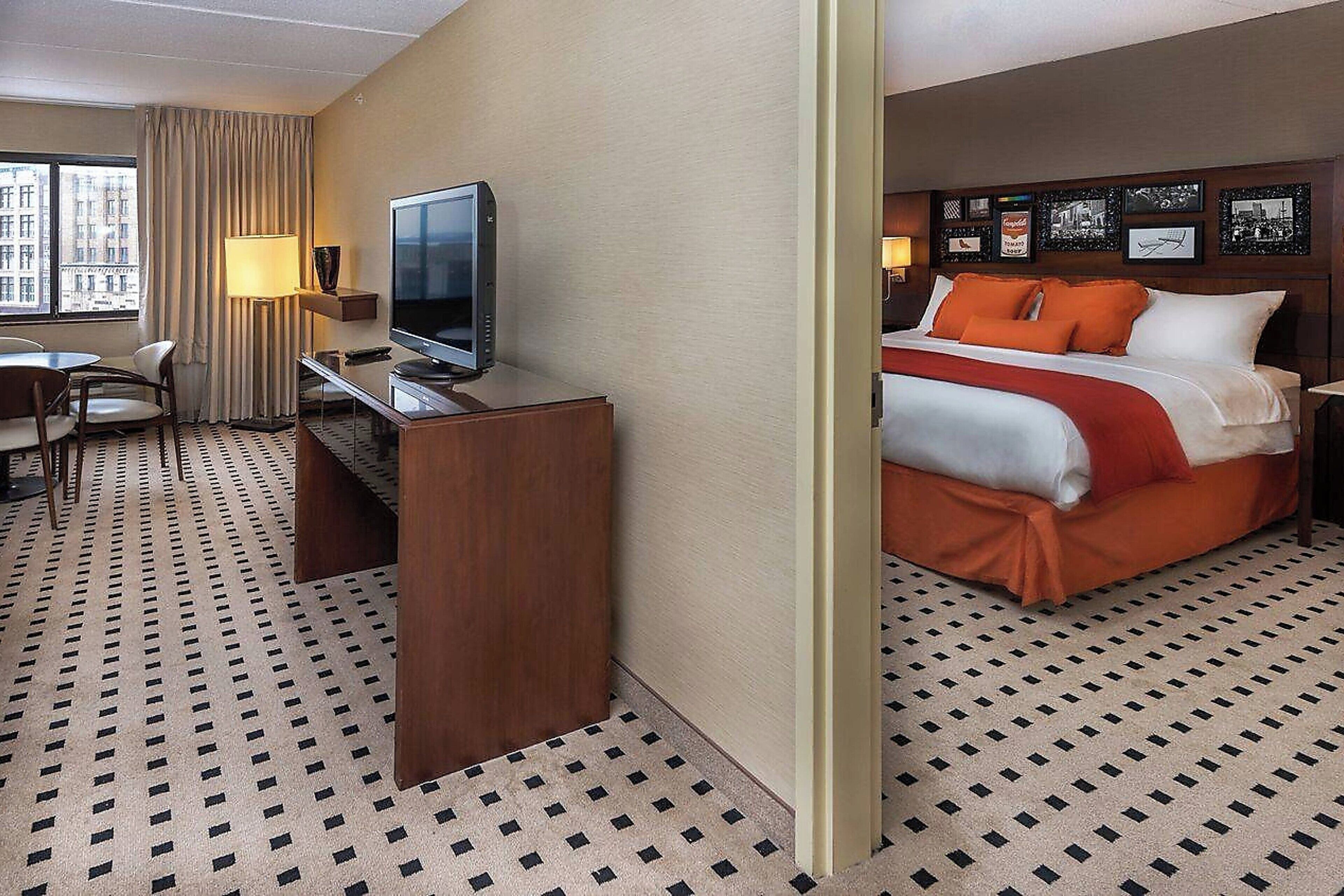 A hotel room with a bed, a desk with a television, a chair, and a window with curtains.