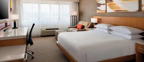 A hotel room with a bed, a desk, a chair, a TV, and a window with curtains.