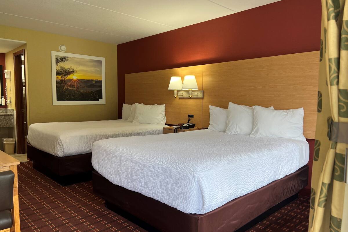 A hotel room with two beds, a desk, a chair, a painting on the wall, and a lamp above the beds.
