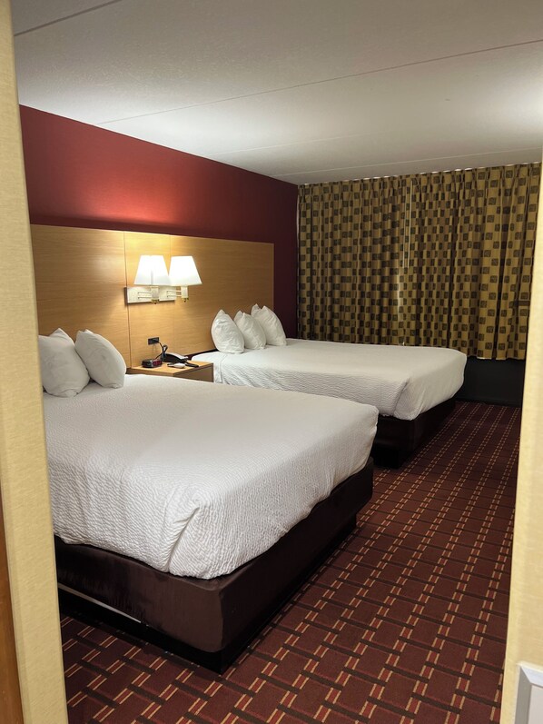 A hotel room with two beds, a headboard with a lamp, a patterned curtain, and a checkered carpet.