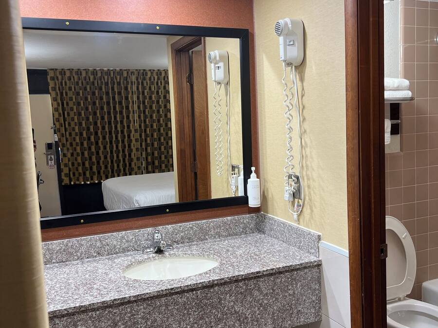 A hotel bathroom with a granite sink, a mirror, a hairdryer, and a toilet.